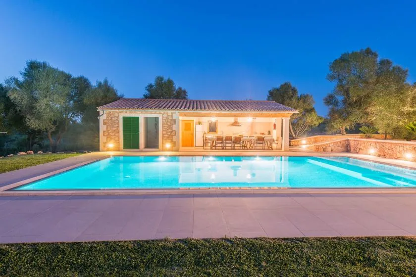 Una piscina frente a una casa, con una zona de comedor al aire libre.