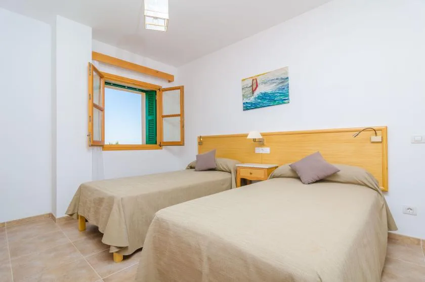 Un dormitorio luminoso con dos camas y una ventana abierta.