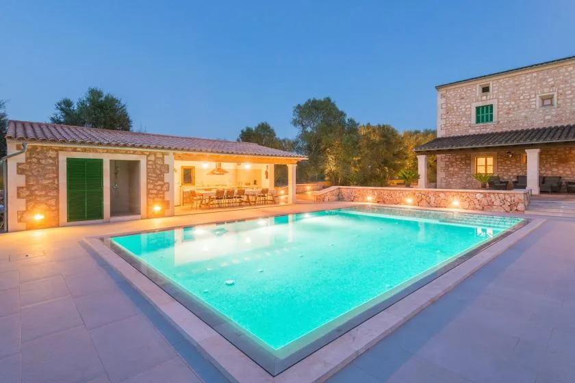 Una piscina al aire libre junto a un edificio de piedra y una zona de asientos cubierta.
