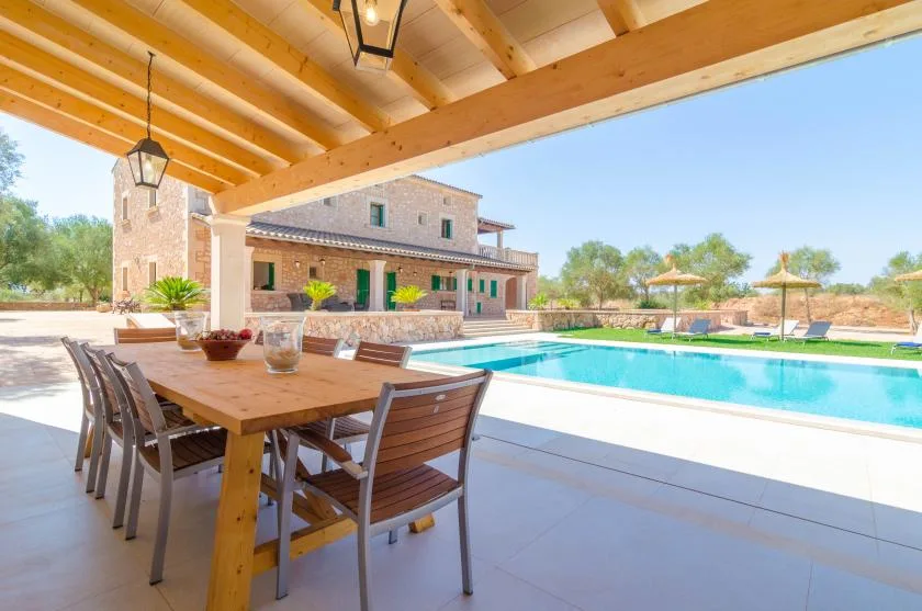 Una zona de comedor exterior cubierta da a una piscina y una casa de piedra.