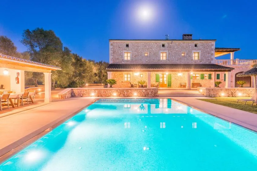 Una piscina frente a un edificio de piedra, con una zona de comedor al aire libre al lado.