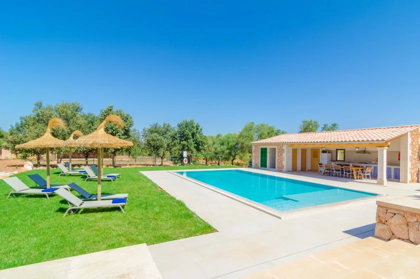 Una piscina al aire libre junto a un patio cubierto, con asientos en el césped.