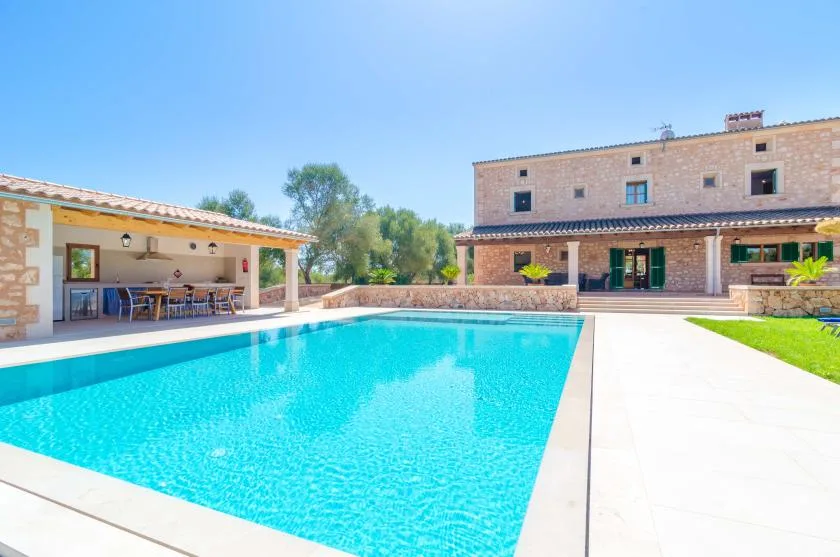 Una piscina al aire libre está junto a una casa de piedra y un patio cubierto.