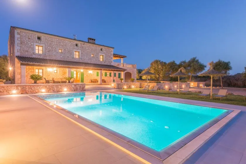 Una casa de piedra se encuentra junto a una piscina exterior iluminada al anochecer.