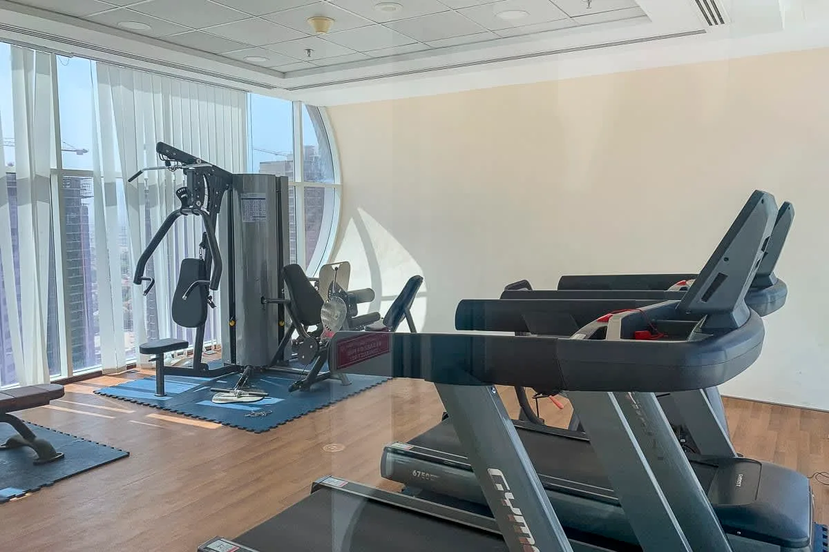 Un gimnasio con cintas de correr y otros equipos de ejercicio junto a grandes ventanas.