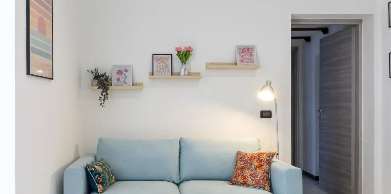 A bright living room with a pale blue sofa and small wall shelves.