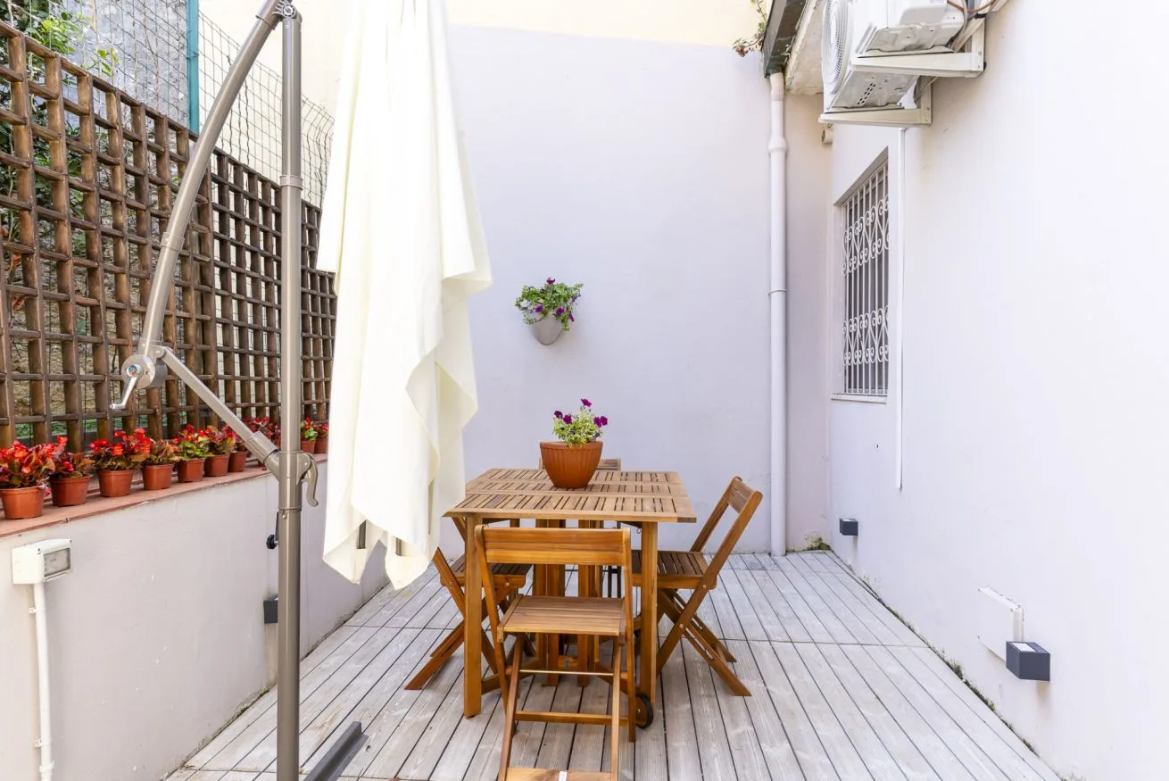 A small outdoor patio with wooden seating and potted flowers.