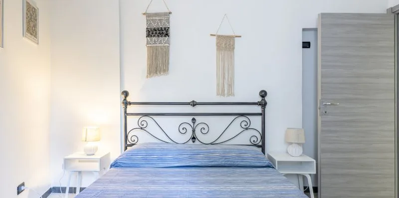 A bedroom with a metal bed and two woven wall hangings.