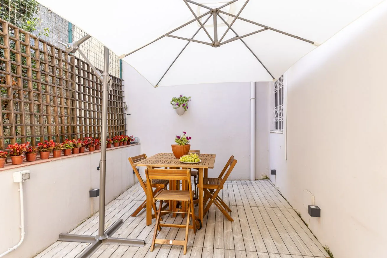 A small outdoor dining area with a wooden table and chairs beneath a large umbrella.
