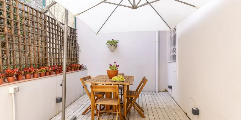 An outdoor patio with a wooden dining table beneath a large umbrella.