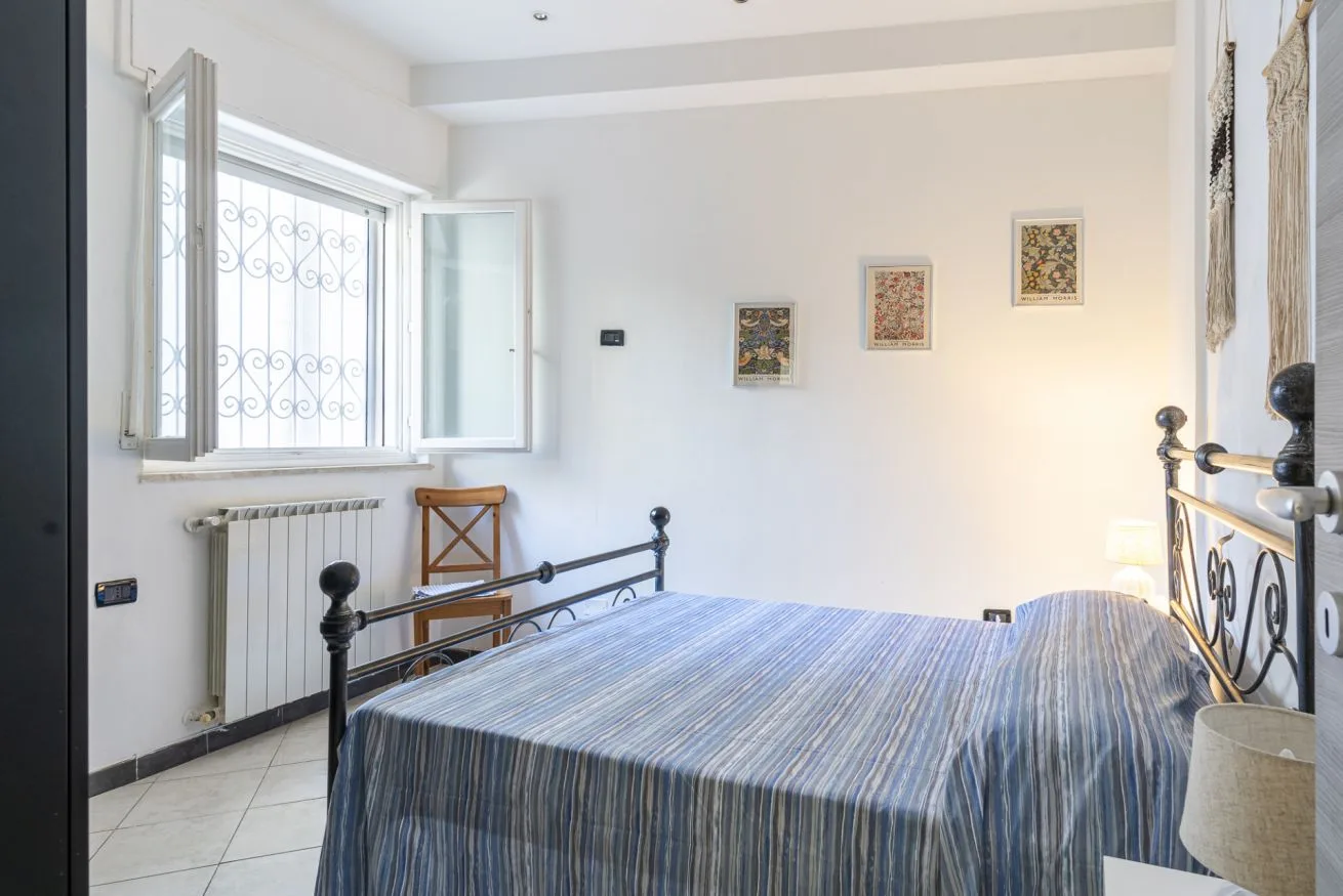 A bedroom with a striped bedspread, an open window, and framed pictures.