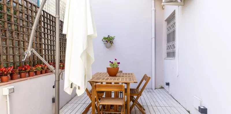 A small outdoor patio with wooden seating, potted flowers, and a white umbrella.