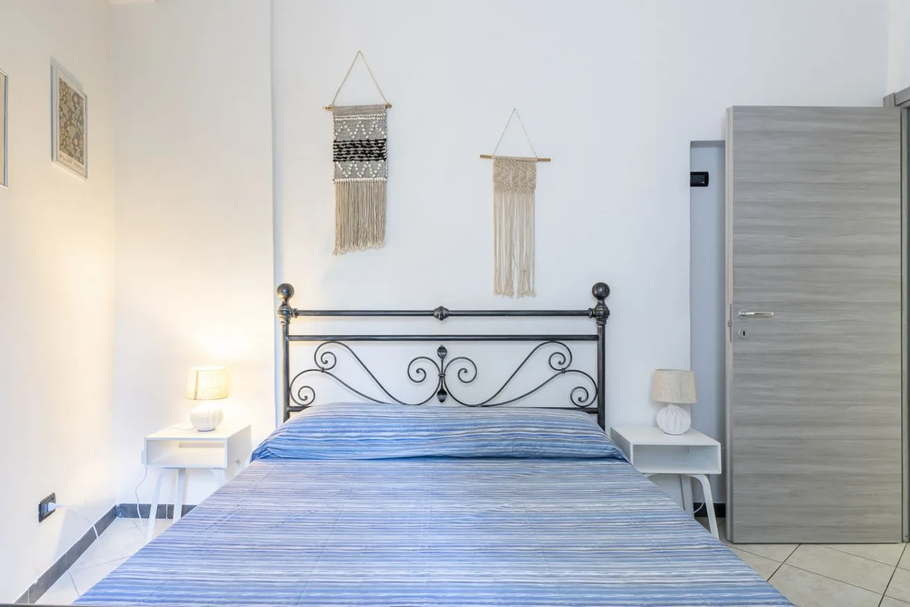 A bedroom with a metal bed, bedside tables, and woven wall hangings.