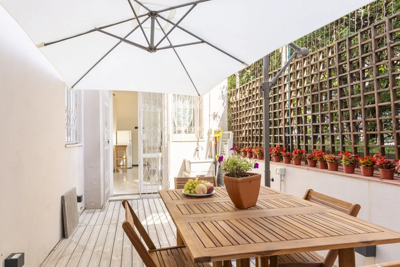 A bright patio with wooden seating, a large canopy, and potted plants along a trellis.