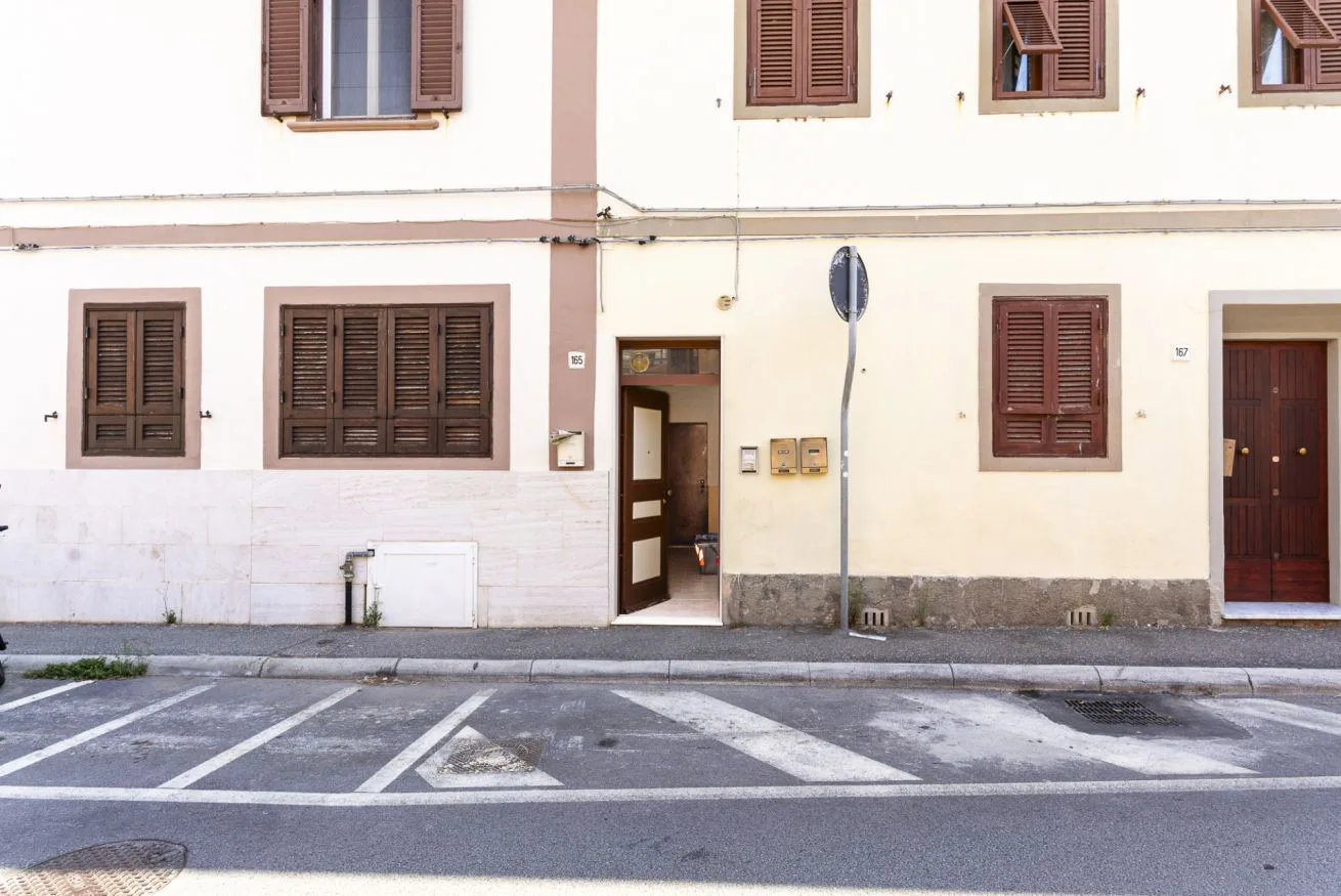 A pale building facade with shuttered windows and street parking markings in front.