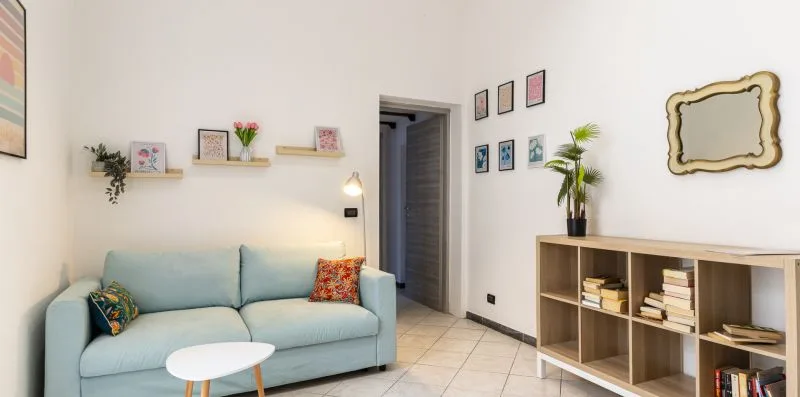 A living room with pale blue seating, wall shelves, and an open doorway.