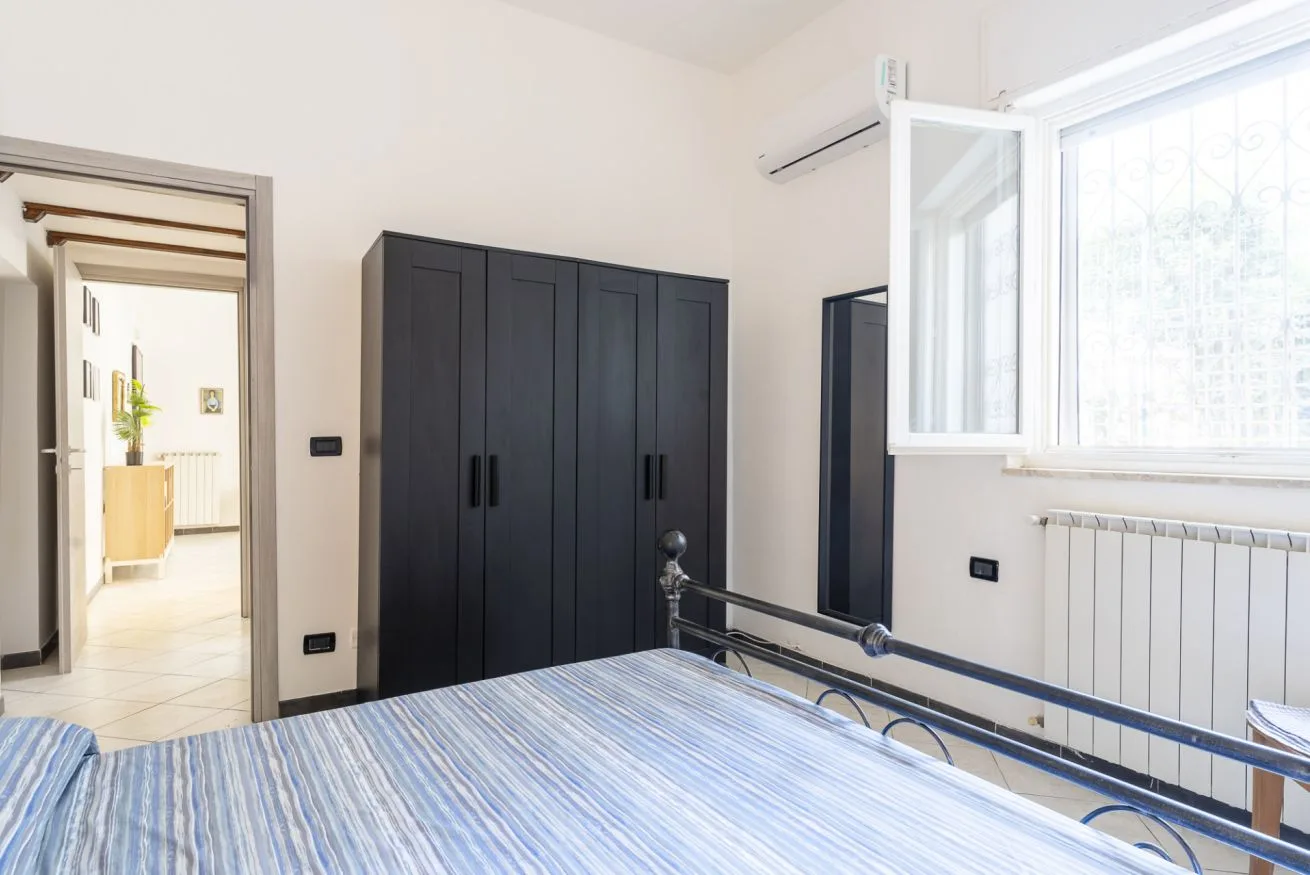A bright bedroom with a bed, dark wardrobes, and an open window.