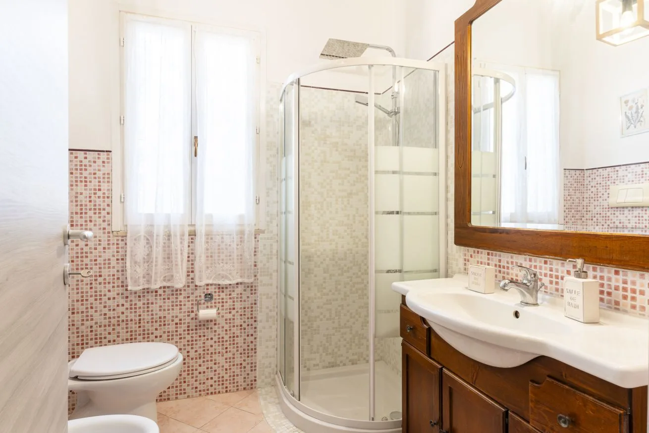 A bright bathroom with a glass shower, a sink, and a window.