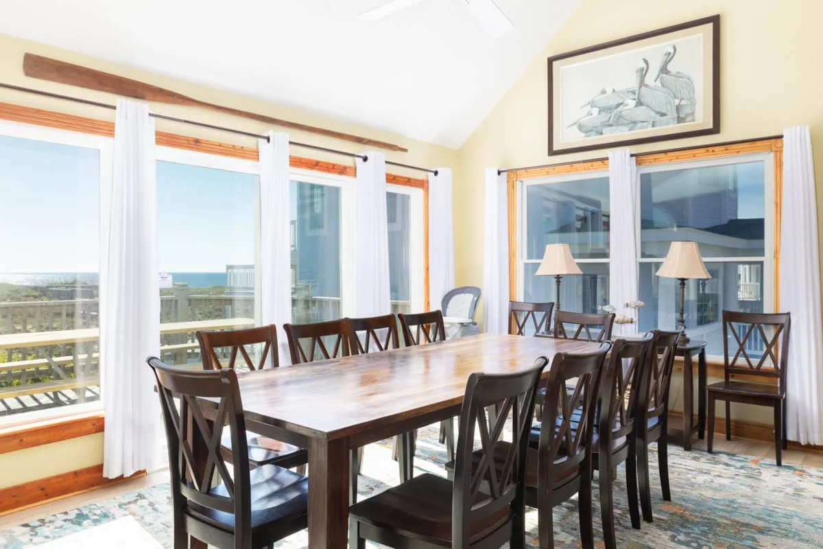 A dining room with a long table and large windows overlooking the water.