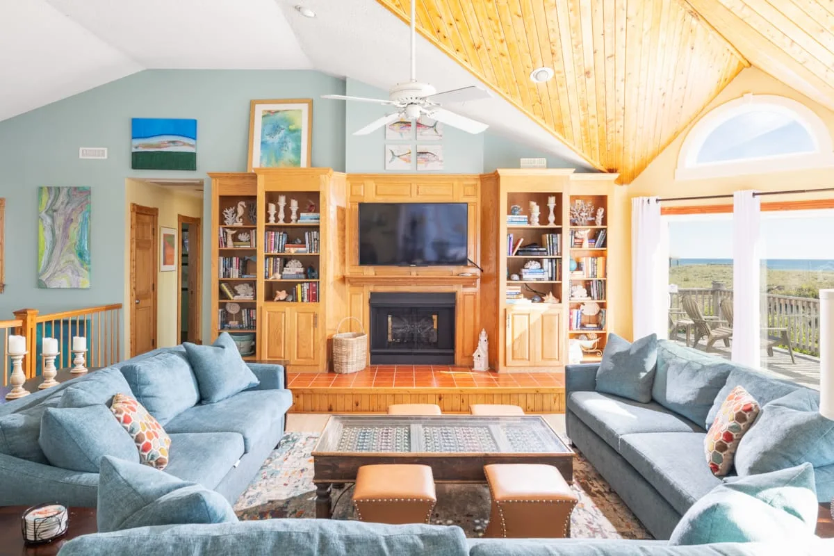 A bright living room with seating, a fireplace, and large windows overlooking a deck.
