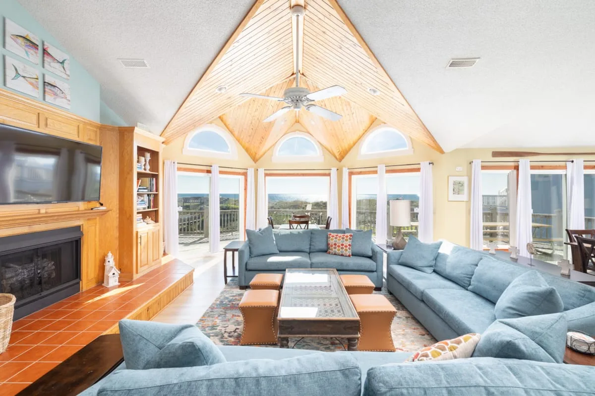 A bright living room has vaulted wood ceilings and seating arranged around a coffee table.