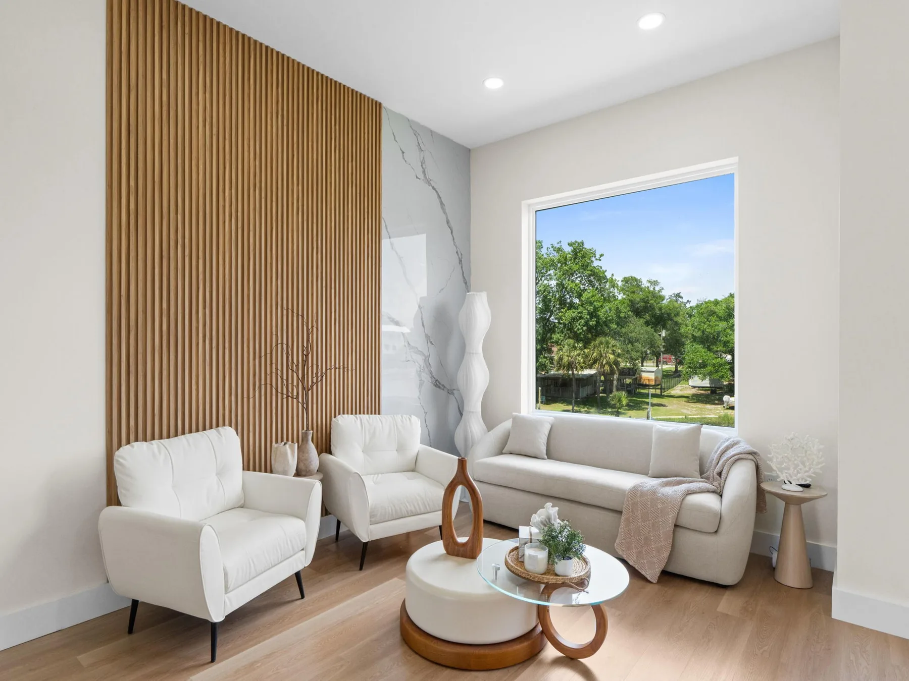A bright living room with white seating and a large window overlooking greenery.