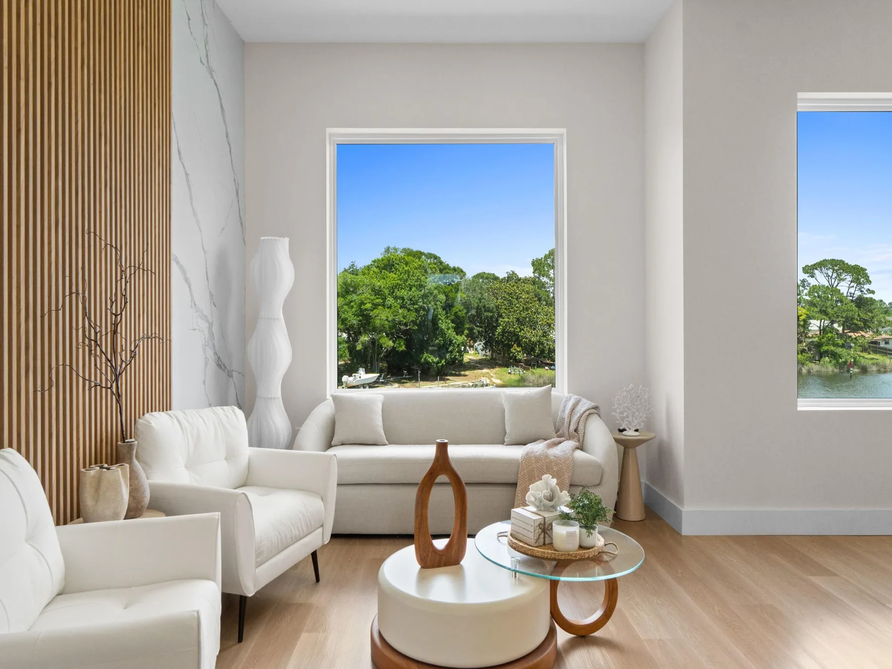 Una sala luminosa con asientos blancos y grandes ventanas con vistas a la vegetación.