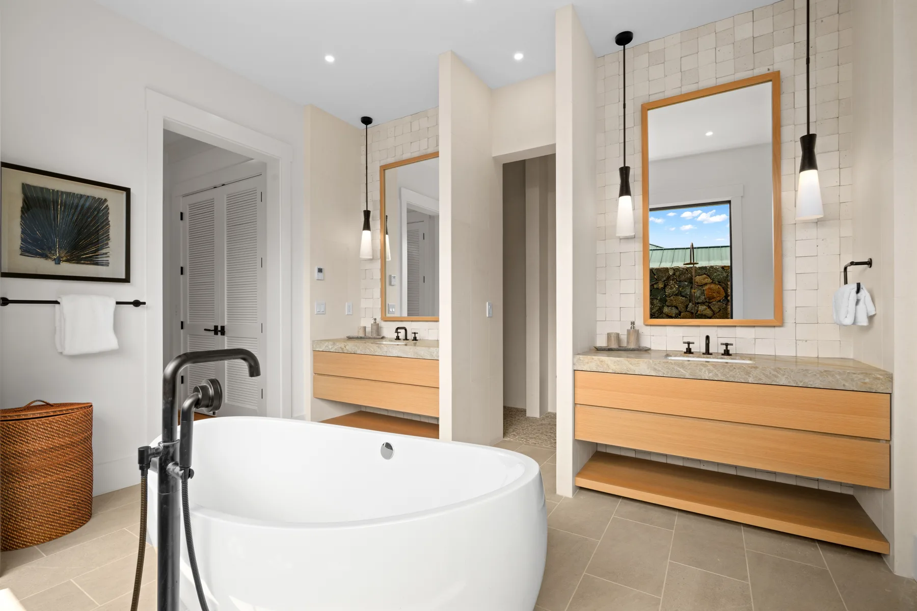 A bright bathroom with a freestanding tub and wood-toned vanities.