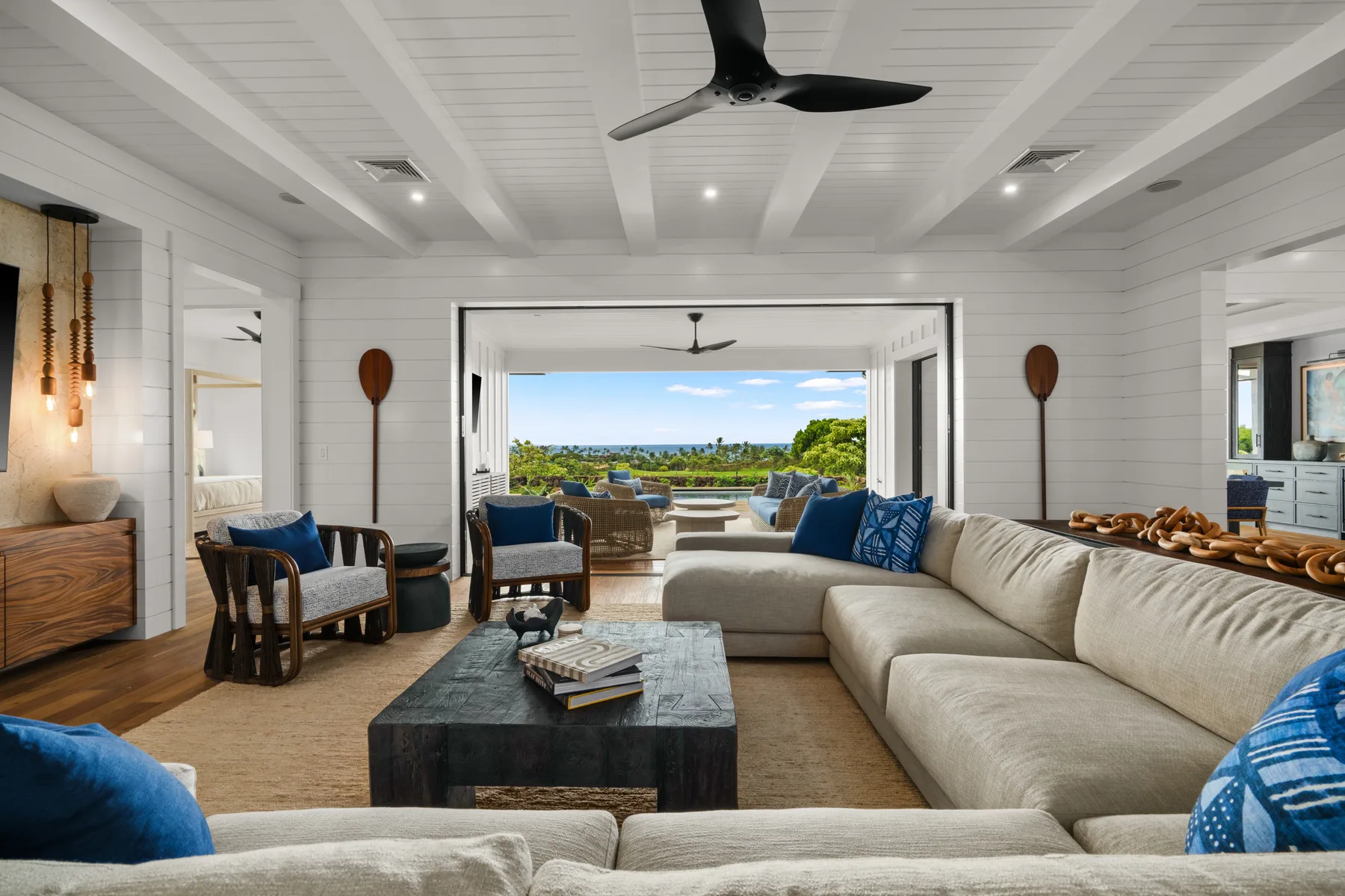 A bright living room with a sectional seating area and open views of greenery and the sea.