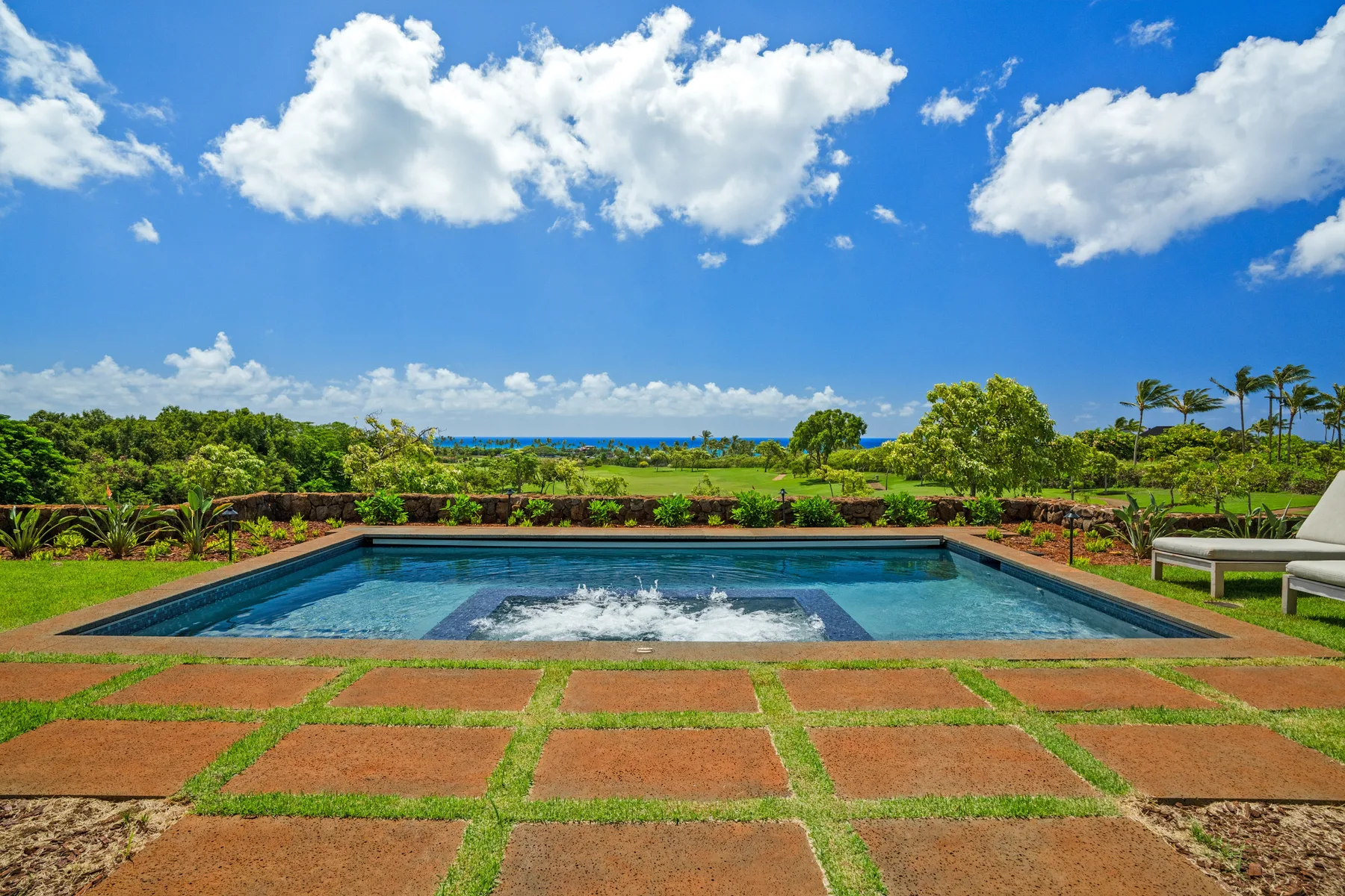 An outdoor swimming pool sits amid landscaped grounds beneath a cloudy blue sky.