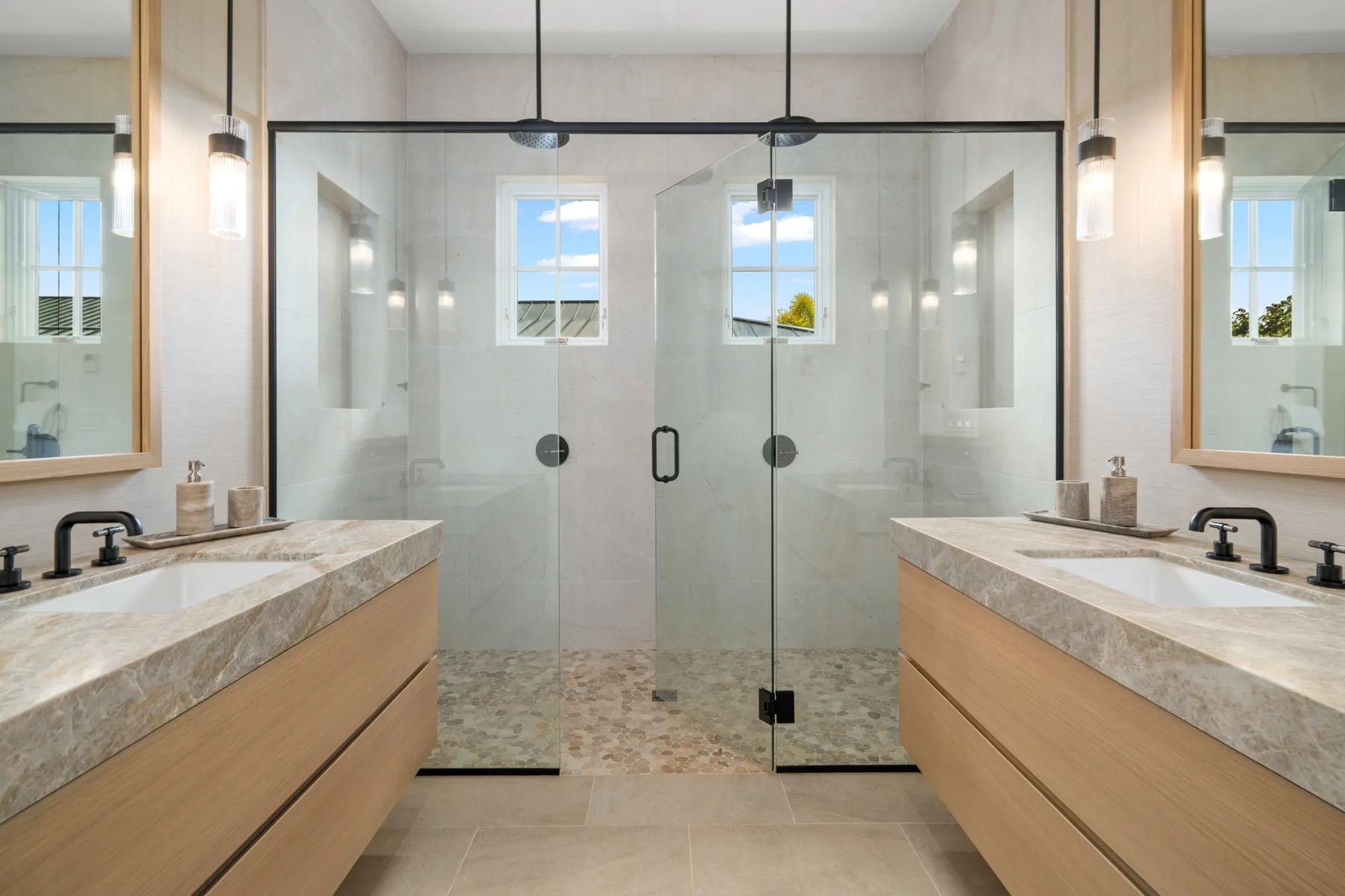 A bright bathroom with a glass-enclosed shower and matching vanities.