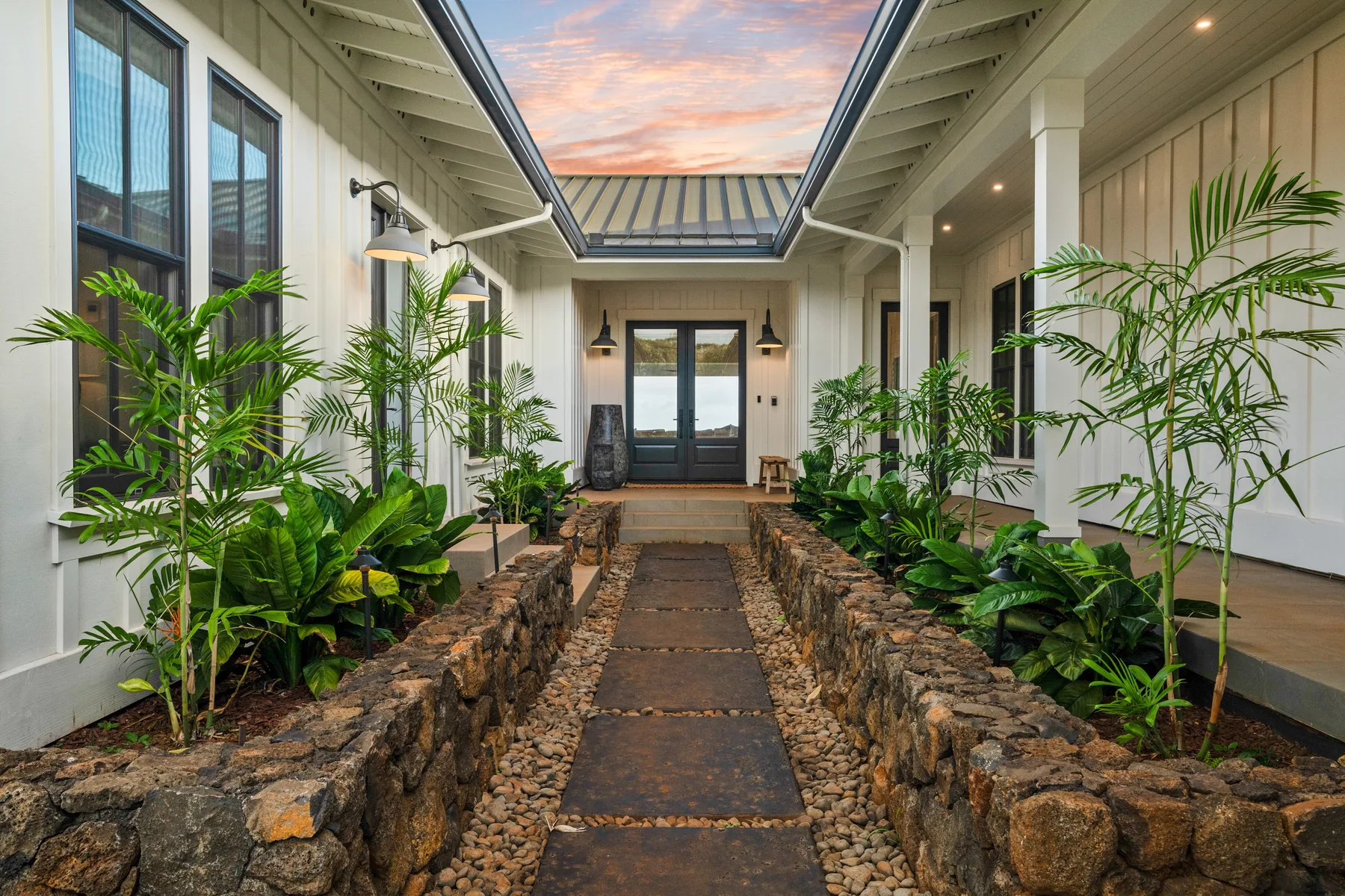 A stone path leads through a planted courtyard toward glass entrance doors.