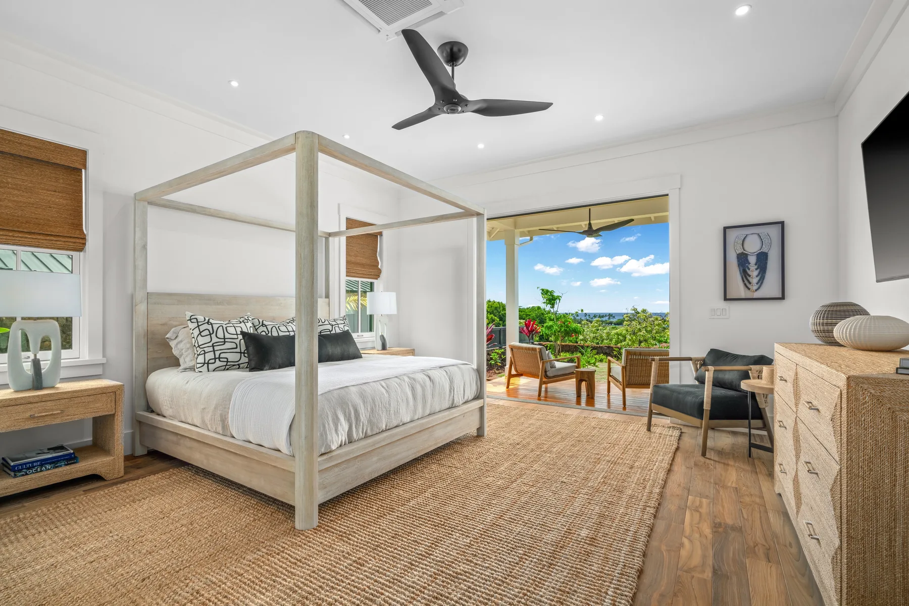 A bright bedroom with a canopy bed and seating beside open balcony doors.