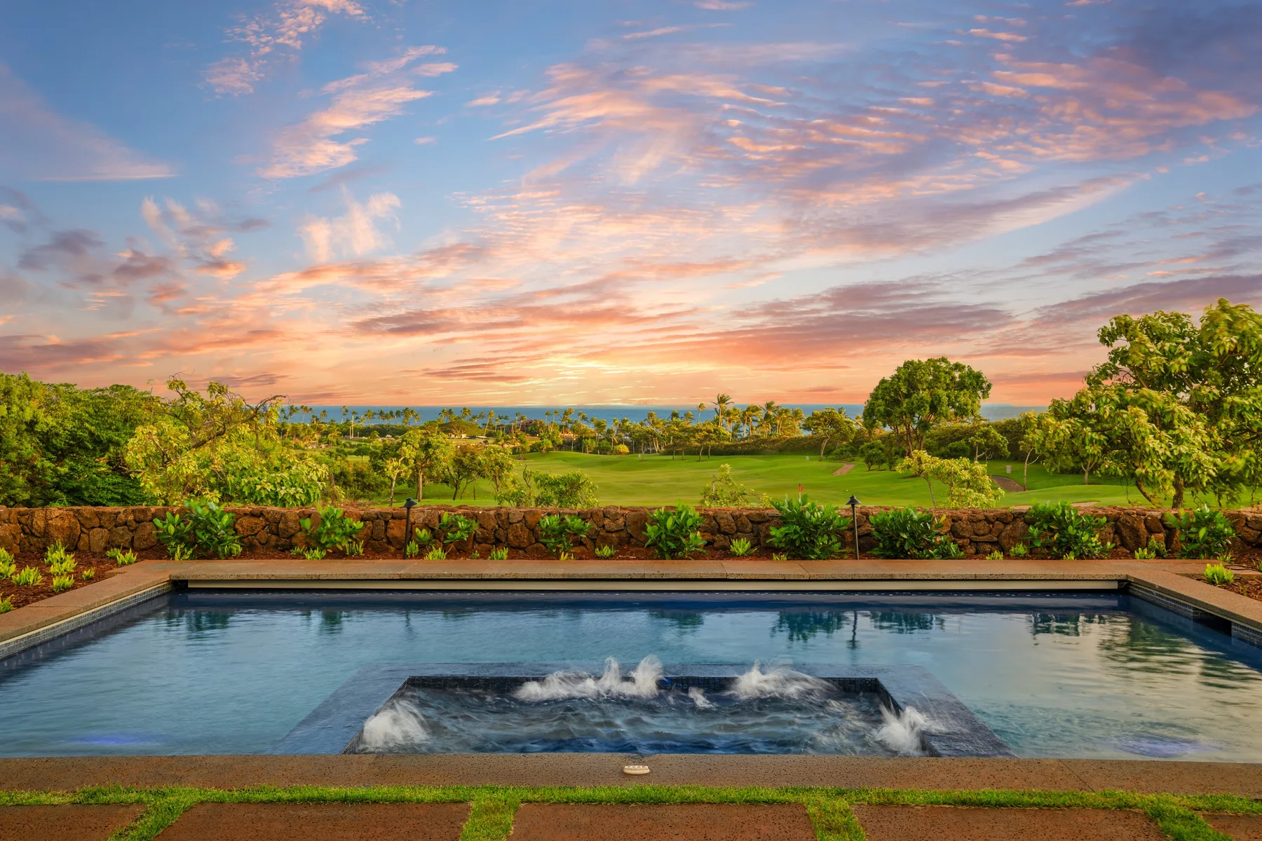 An outdoor pool overlooks a green landscape beneath a colorful sunset sky.