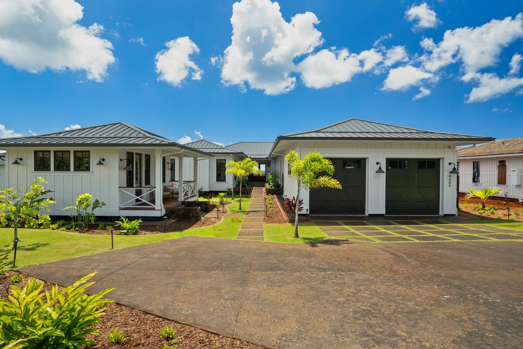 A paved driveway leads to low houses with a garage and landscaped gardens.