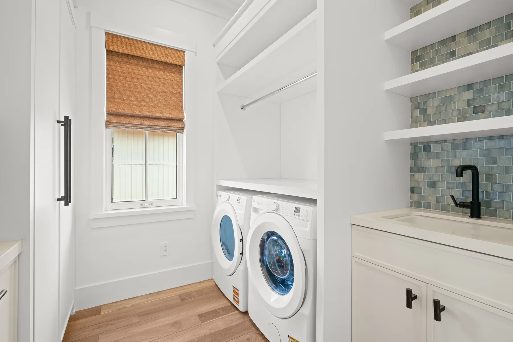 A bright laundry room with a window, washing machines, and a utility sink.