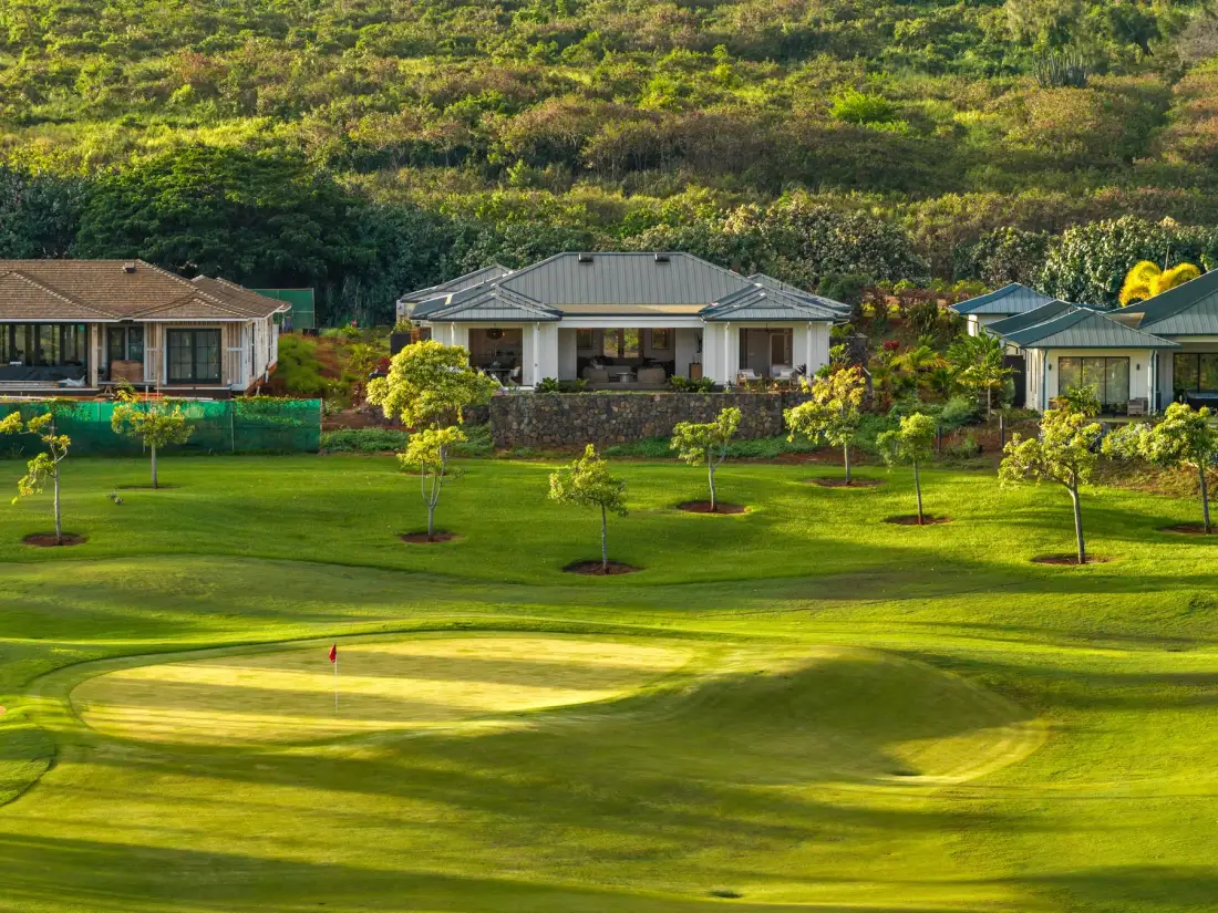 A manicured golf course with a putting green sits in front of hillside homes.
