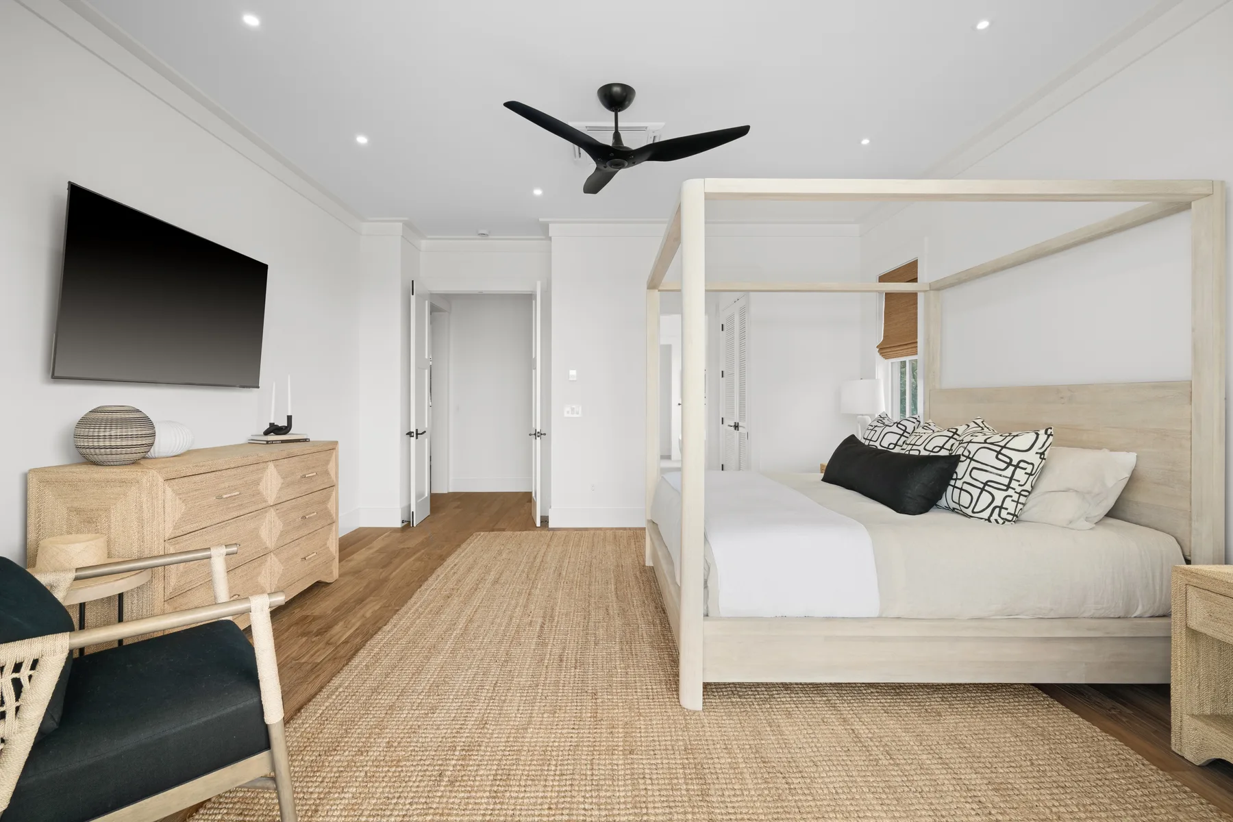 A bright bedroom with a four-poster bed, woven rug, and wall-mounted television.