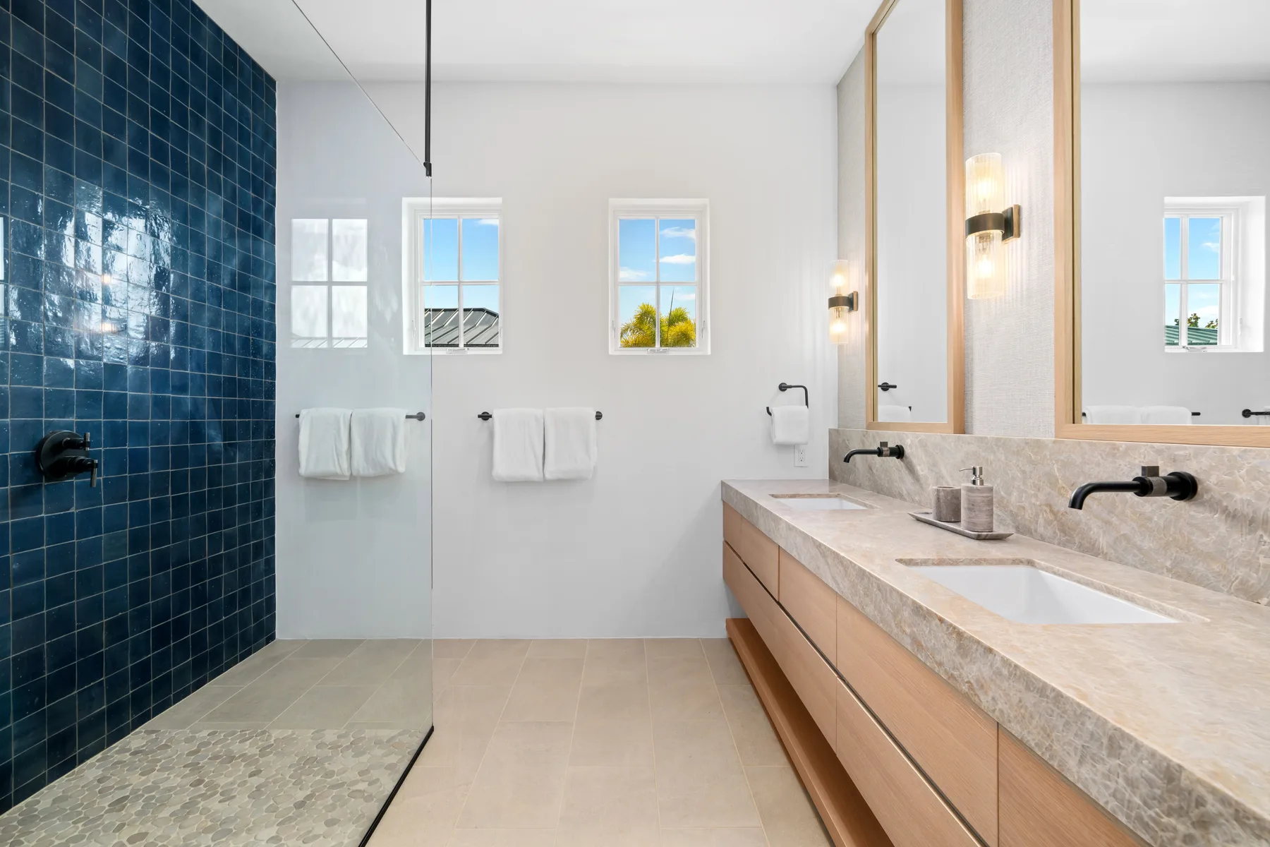 A bright bathroom with a glass shower and a long vanity.