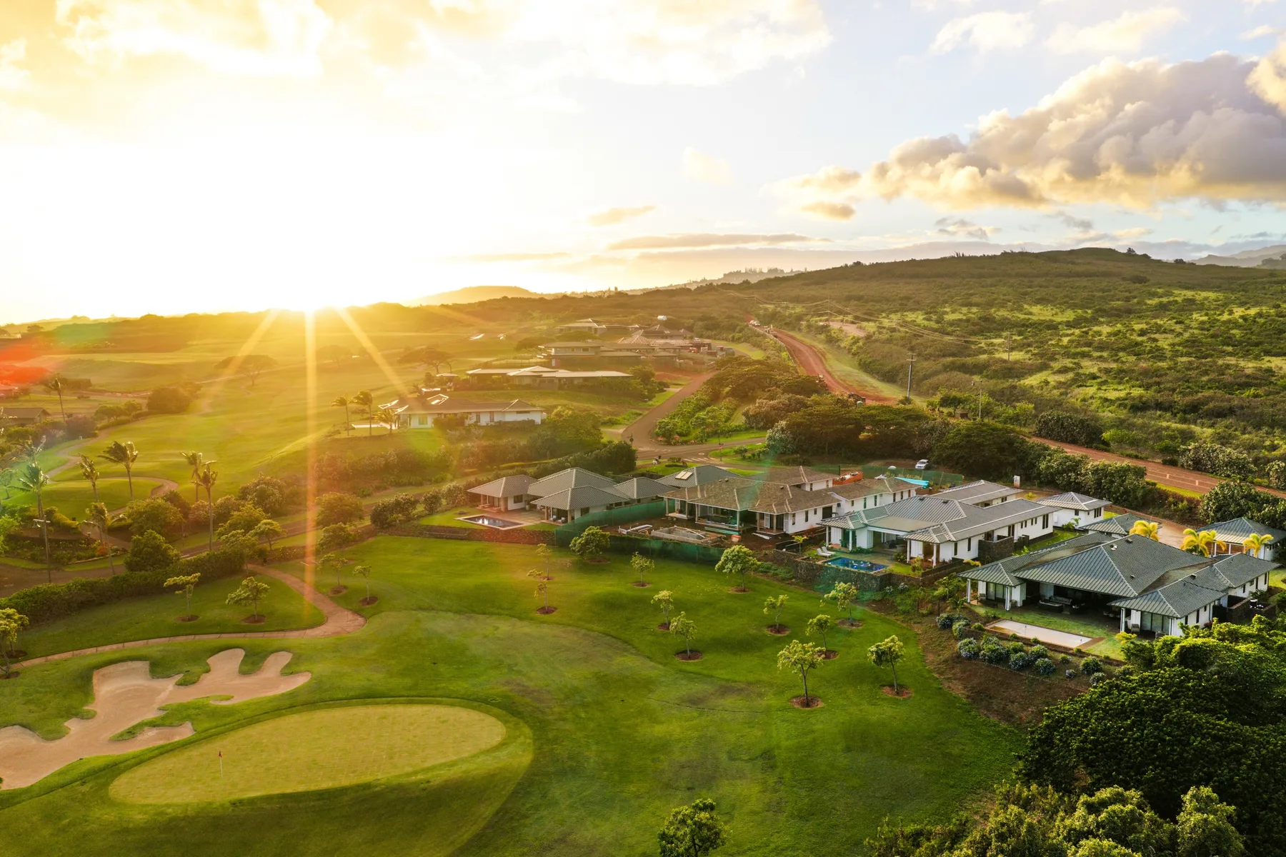 A golf course and resort buildings spread across a green landscape at sunset.