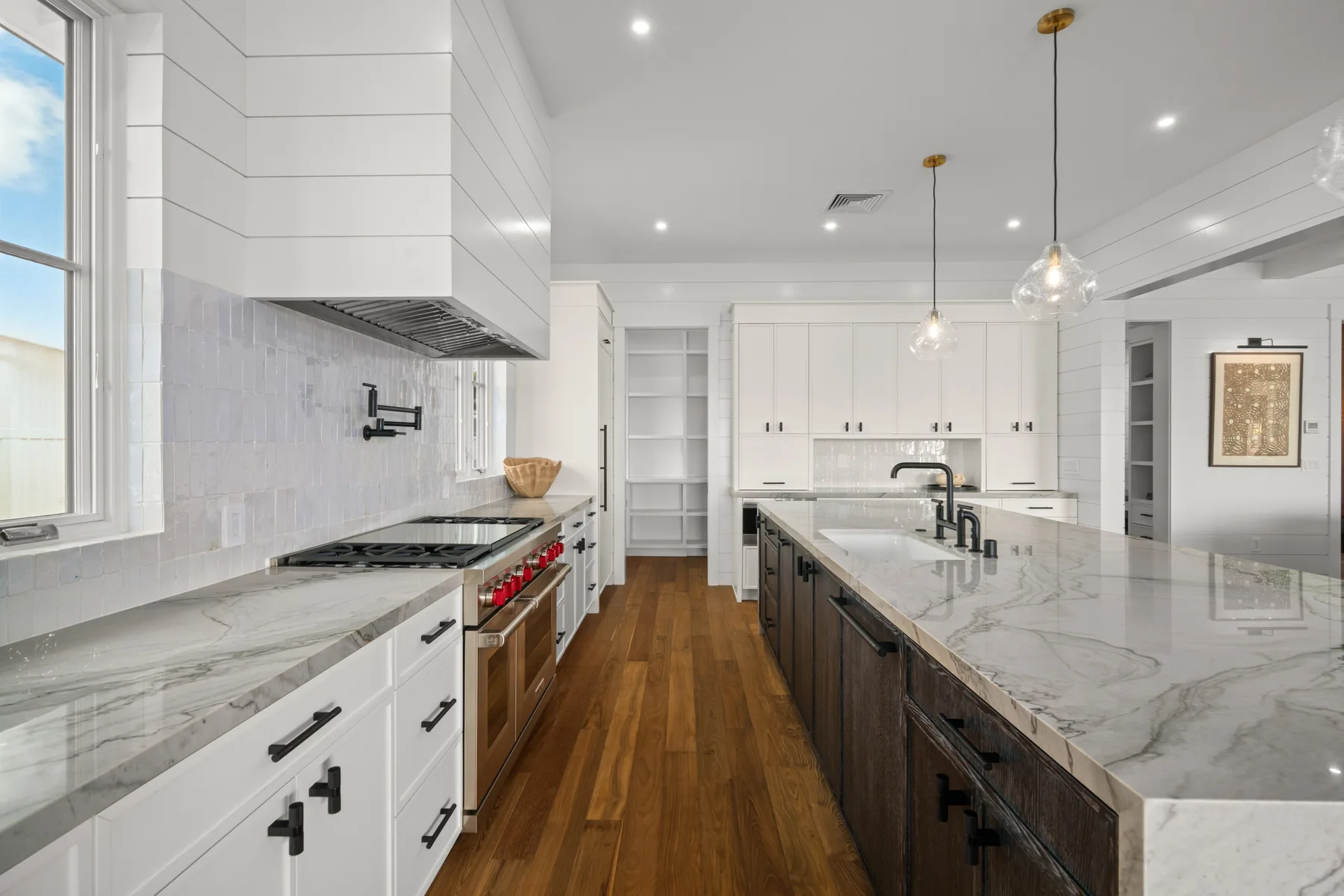 A bright kitchen with a long island, white cabinetry, and wood flooring.