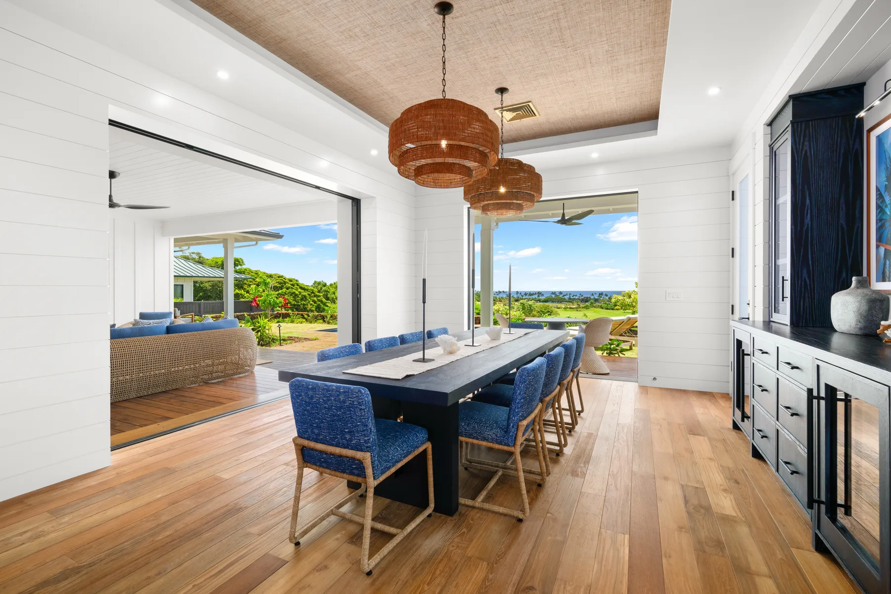 A bright dining area with blue seating and wide openings to a leafy outdoor terrace.