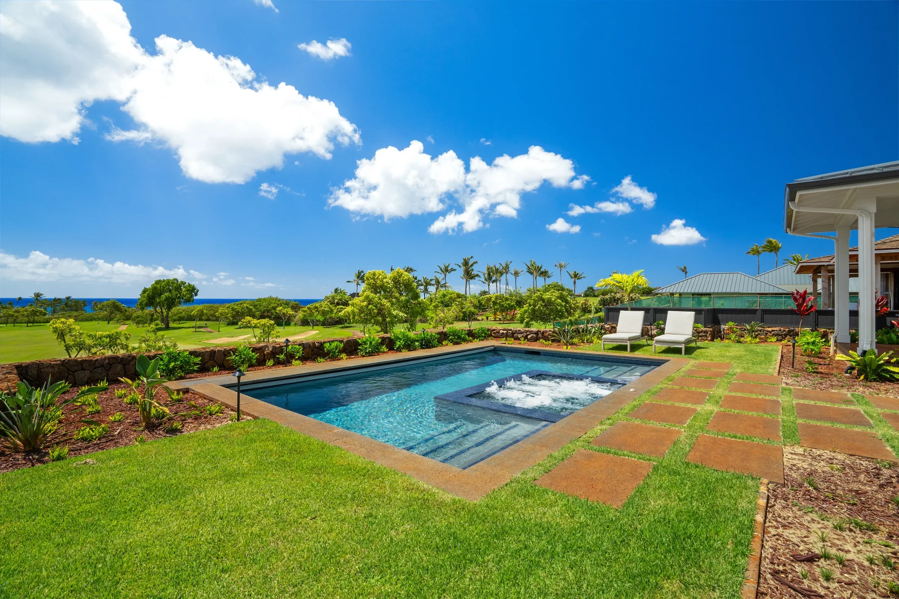 An outdoor swimming pool sits amid green lawns and tropical landscaping.