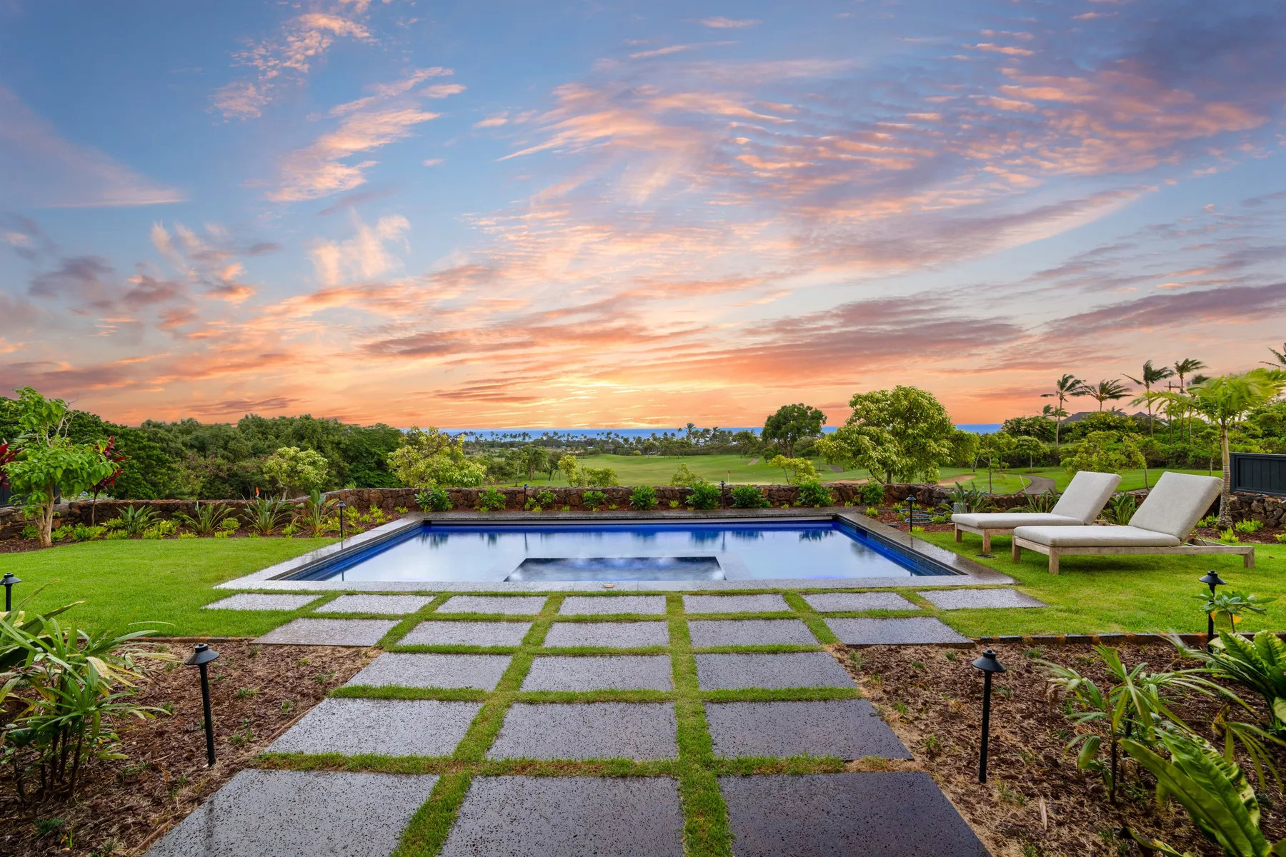 A landscaped garden features a swimming pool and lounge seating beneath a colorful sunset sky.