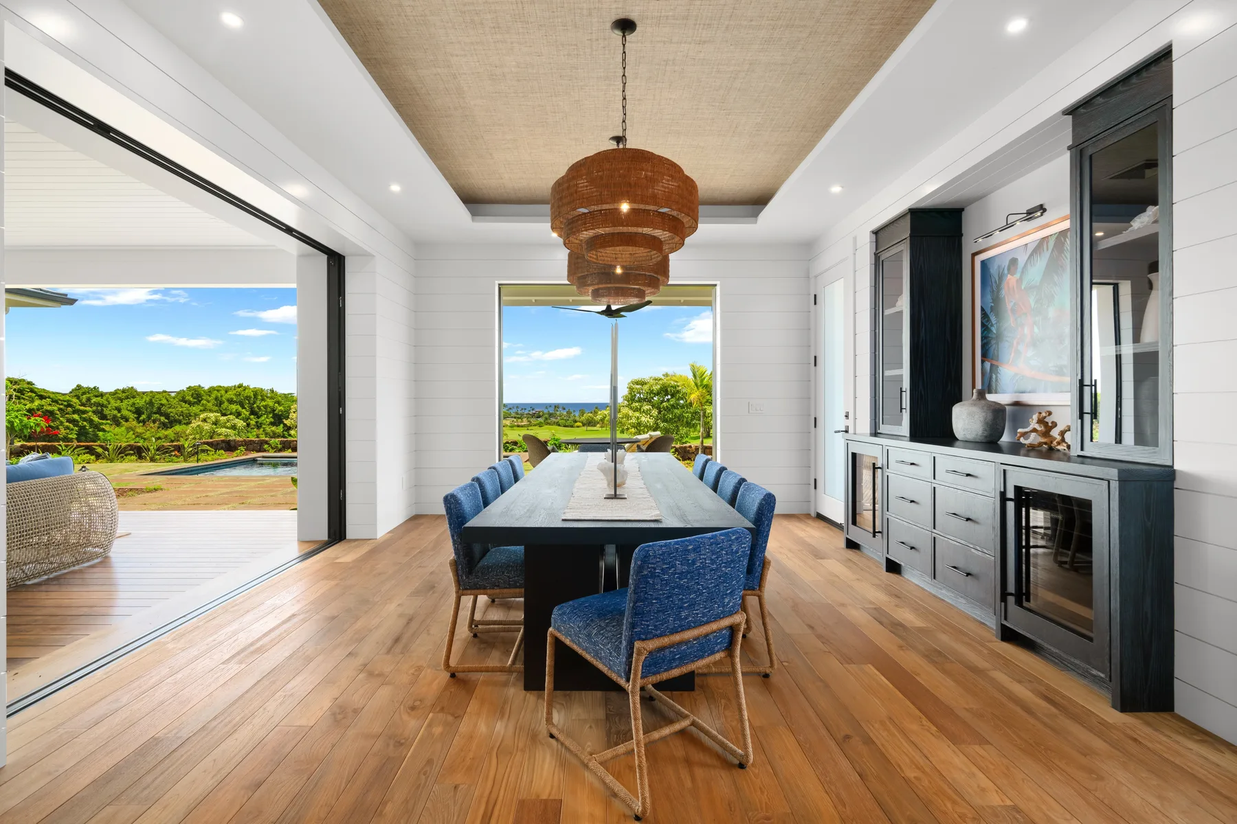 A bright dining area opens onto a patio, with a long table and blue seating.