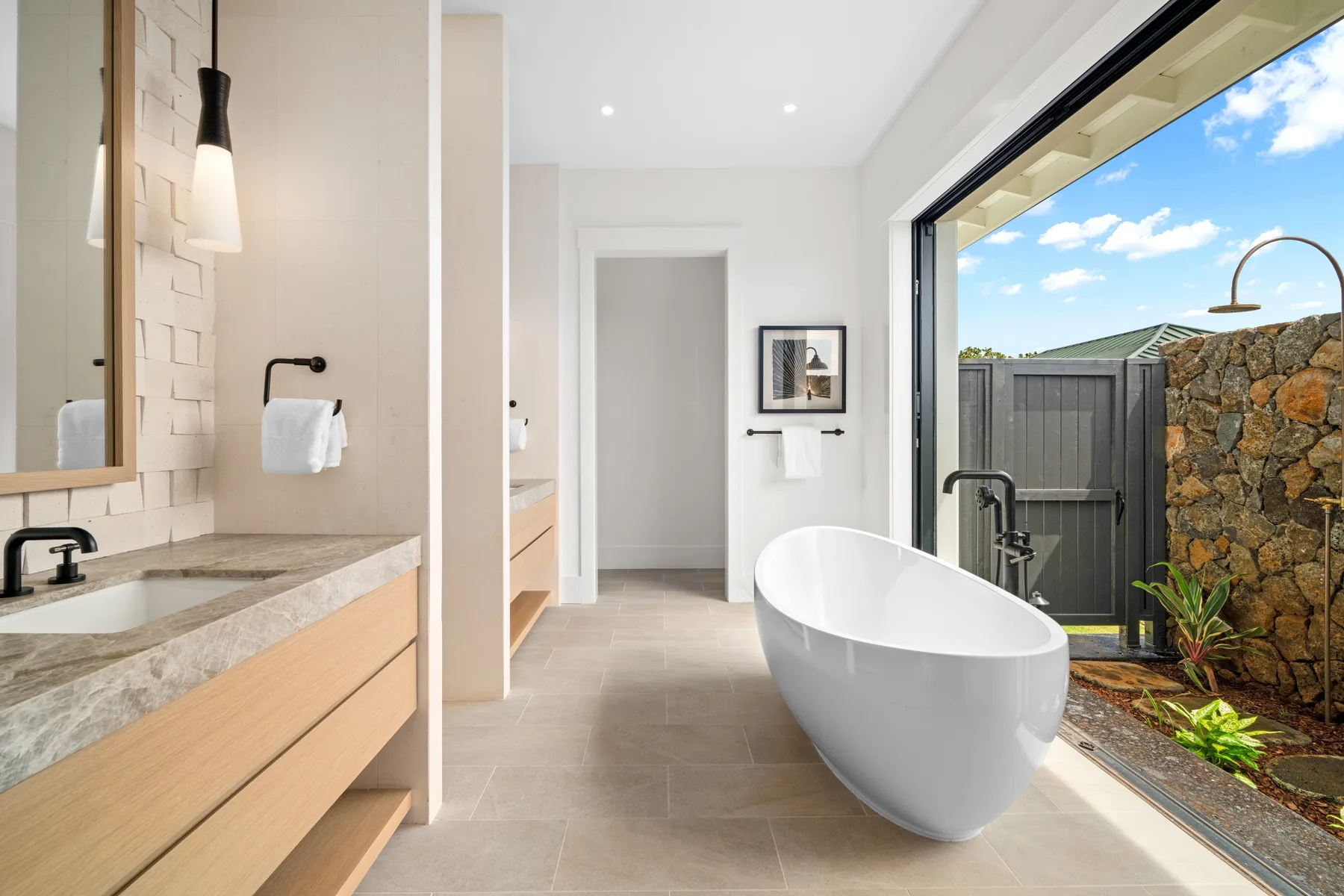 A bright bathroom with a freestanding bathtub beside a large glass opening.