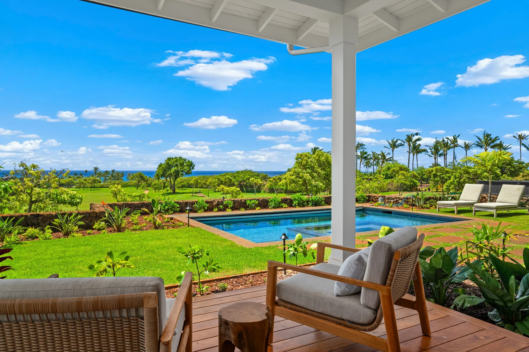 A covered outdoor seating area overlooks a lawn, garden, and swimming pool.