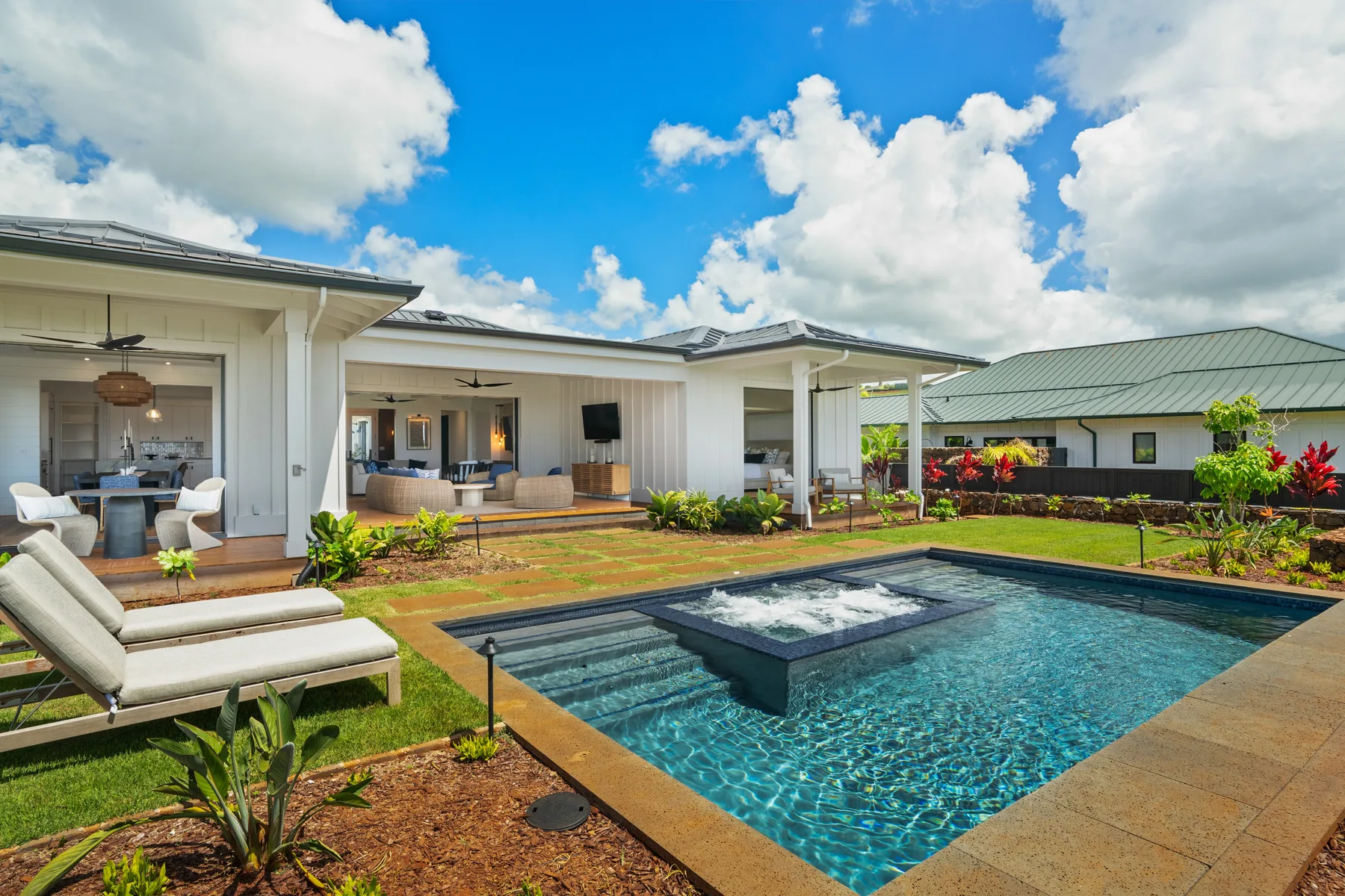 A landscaped outdoor pool sits beside a patio with seating and a covered dining area.