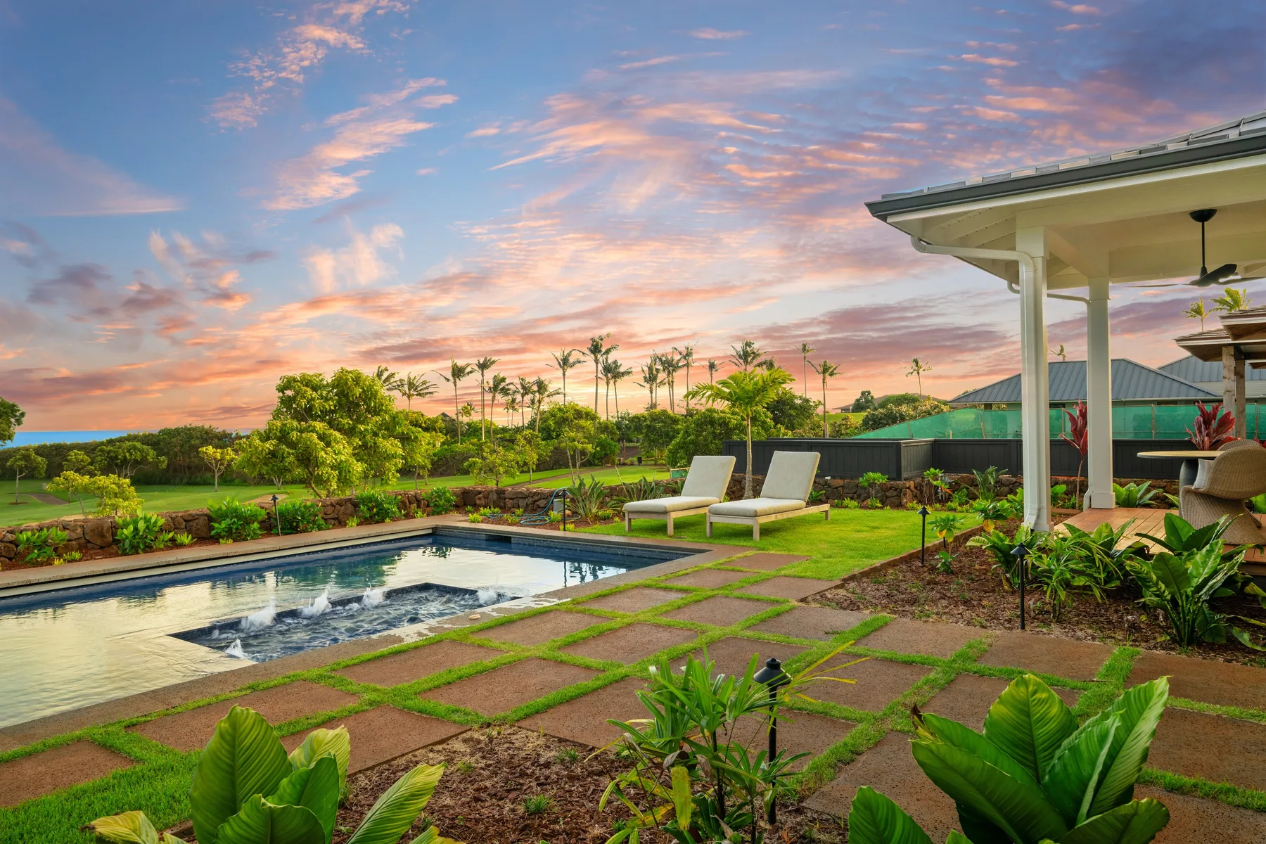 A landscaped outdoor pool sits beside a covered patio beneath a colorful sunset sky.