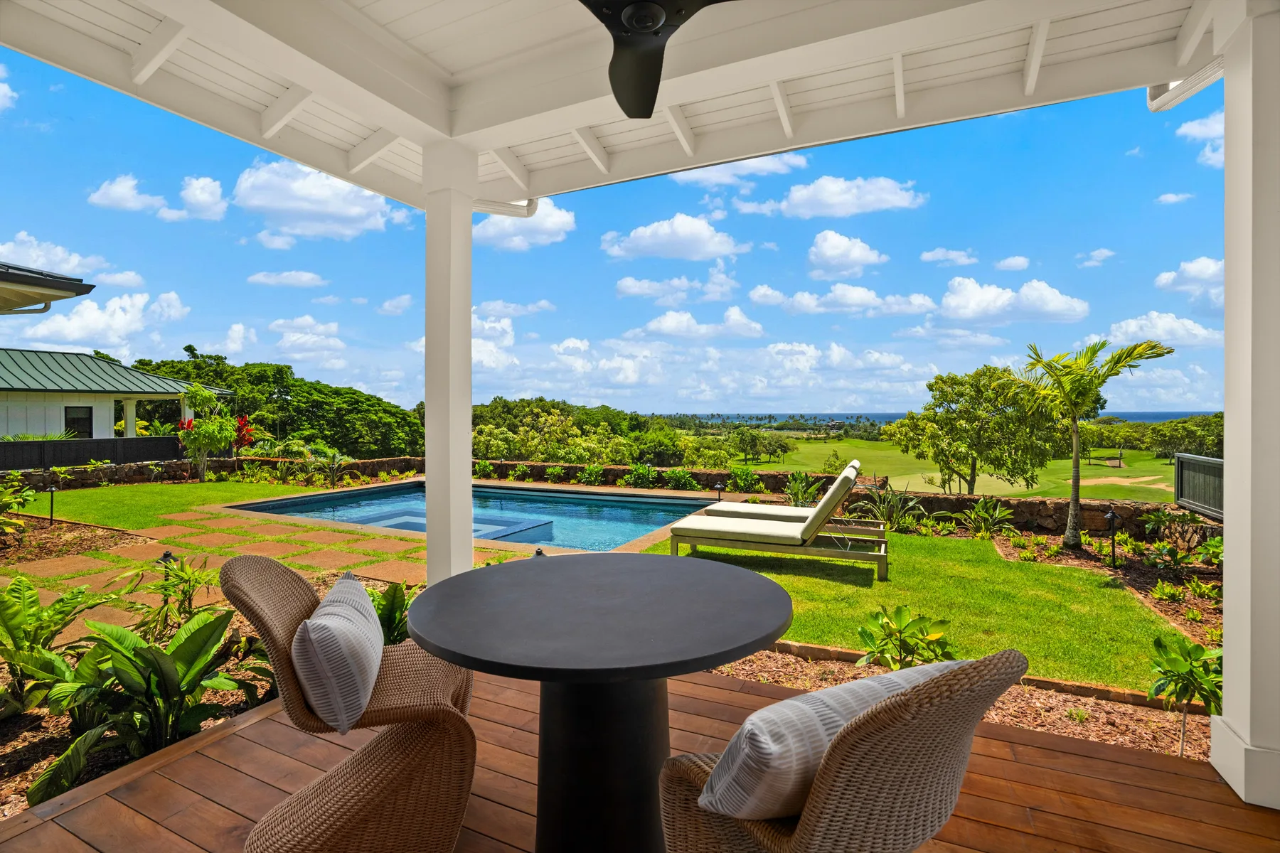 A covered patio with outdoor seating overlooks a swimming pool and garden.